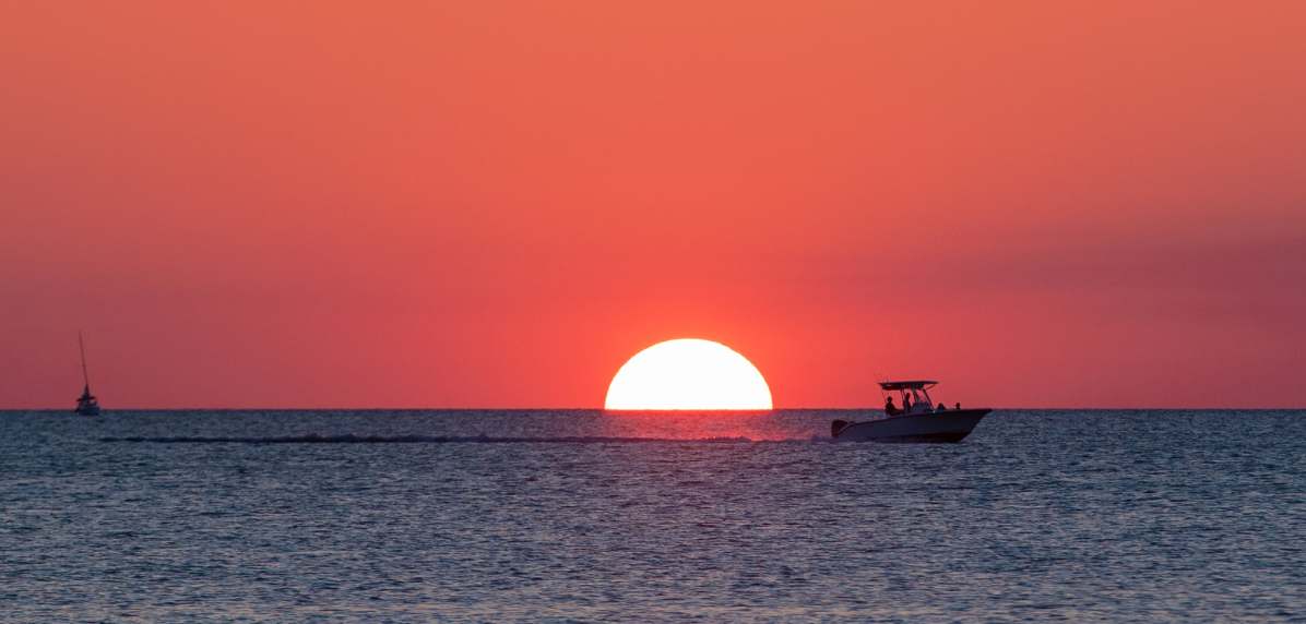 A boat silhouetted against a vibrant sunset on the ocean horizon.